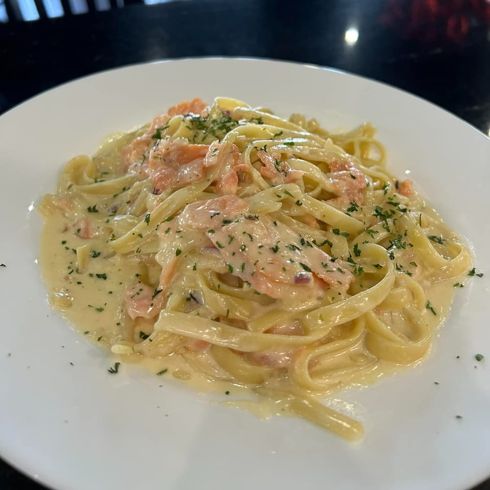 Creamy fettuccine pasta with salmon and parsley on a white plate at The Palazzo Ristorante.