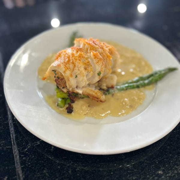 A white plate holds a stuffed lobster tail with asparagus and a creamy sauce.