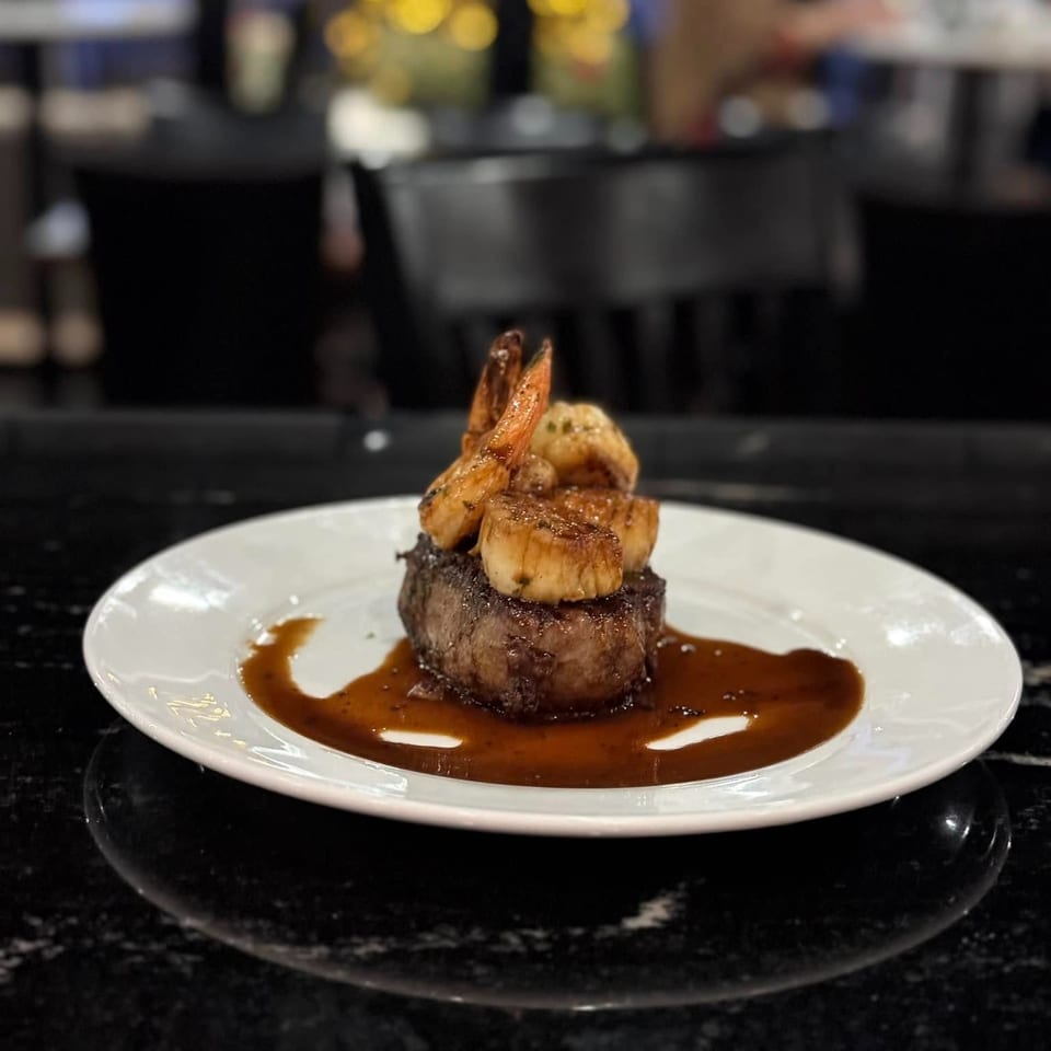 A filet mignon topped with grilled shrimp and scallops, drizzled with a rich brown sauce.
