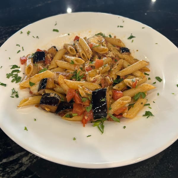 Penne pasta with eggplant, tomatoes, and herbs on a white plate at The Palazzo Ristorante.