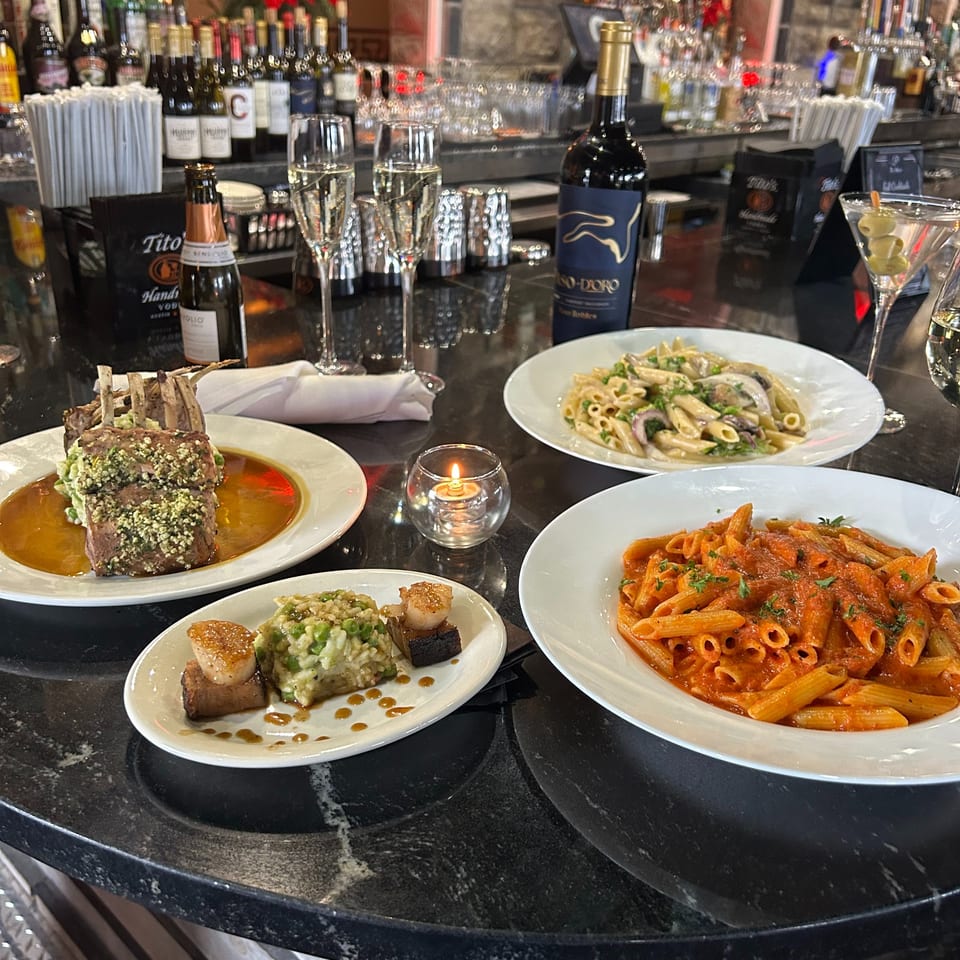 Italian dishes including lamb chops, risotto, and two pasta plates on a black marble bar.