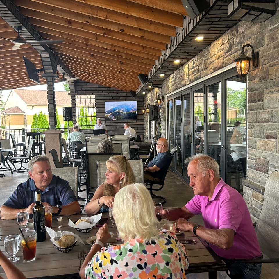 Patrons dining al fresco on The Palazzo Ristorante's covered patio with stone walls and wooden ceiling.