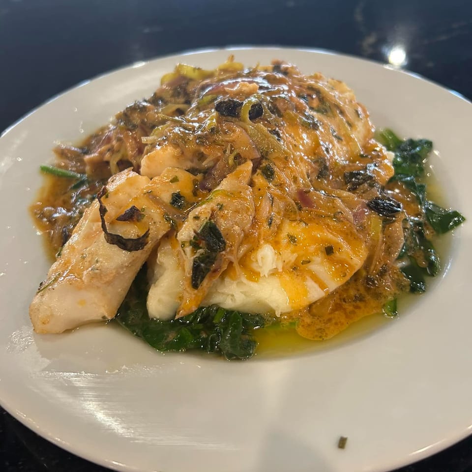 Italian fish dish with sauce, herbs, and spinach on a white plate at The Palazzo Ristorante.