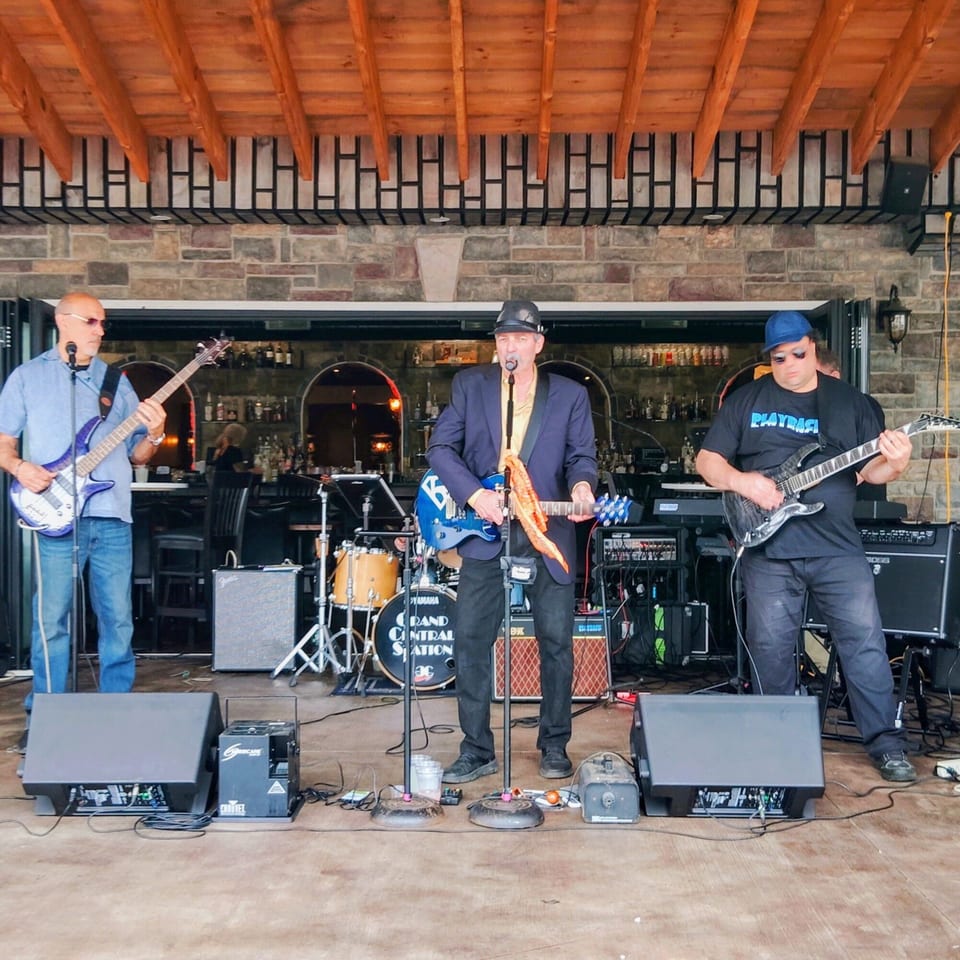 Three musicians performing live on a stage with instruments and sound equipment at The Palazzo Ristorante.