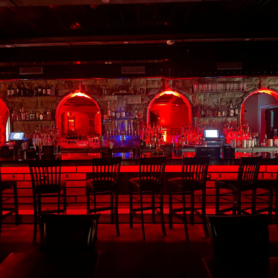 The Palazzo Ristorante's bar glows with red lighting, featuring bottles, glasses, and bar stools.