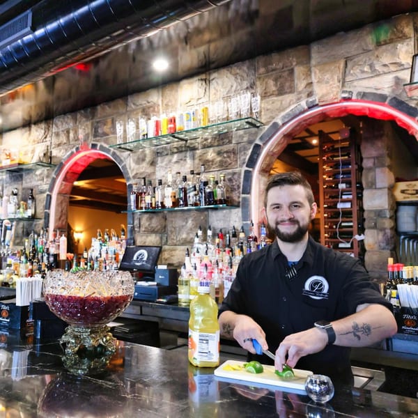 A smiling bartender at The Palazzo Ristorante slices limes behind a bar with a punch bowl.