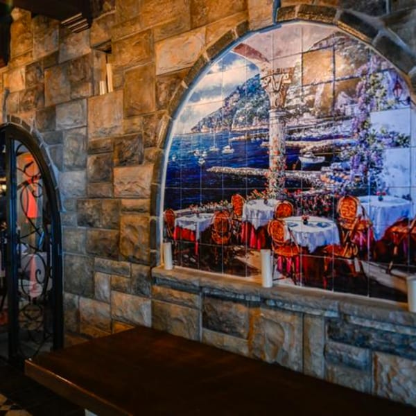 Stone wall with an arched tile mural depicting a coastal Italian town with outdoor dining.