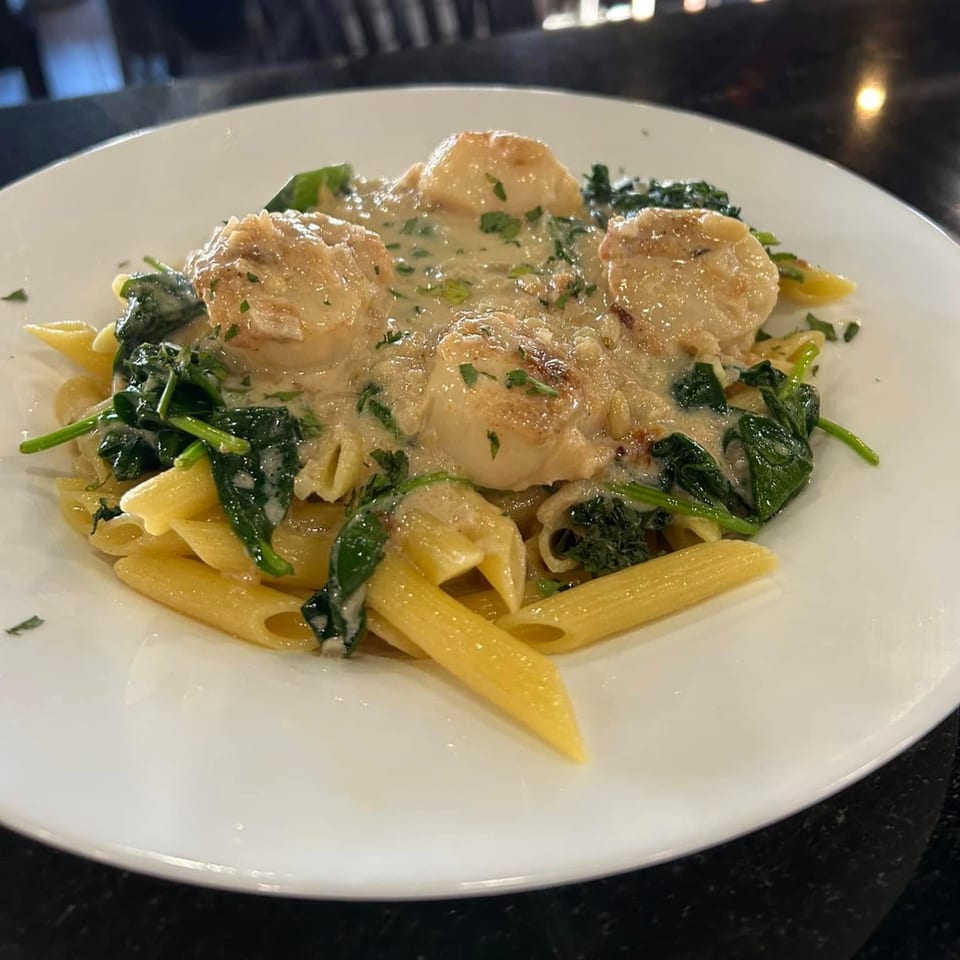 Creamy penne pasta with scallops and spinach, garnished with fresh herbs at The Palazzo Ristorante.