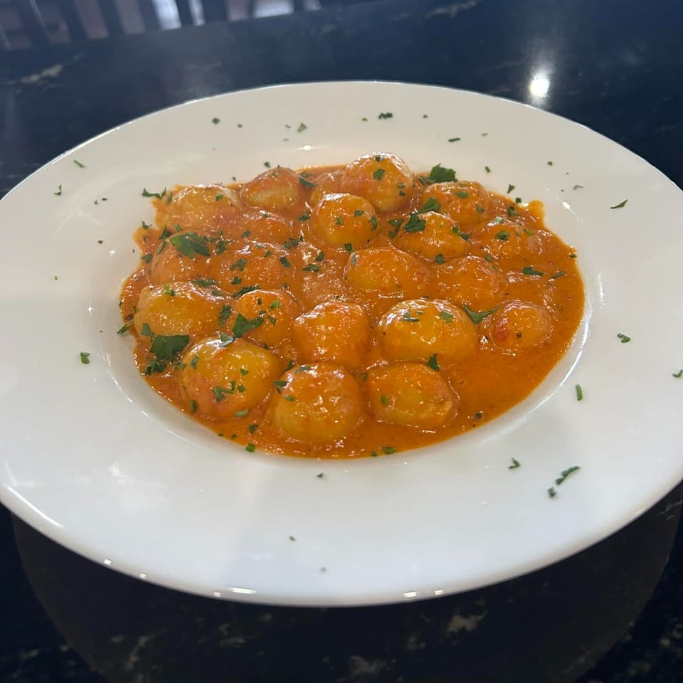 A white bowl of gnocchi in a creamy red sauce, garnished with fresh parsley.